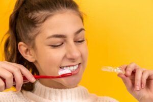 fille souriante en pull blanc tenant une brosse à dents rouge et blanche