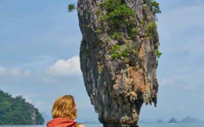 femme en robe rouge assise sur une formation rocheuse près d'un plan d'eau pendant la journée